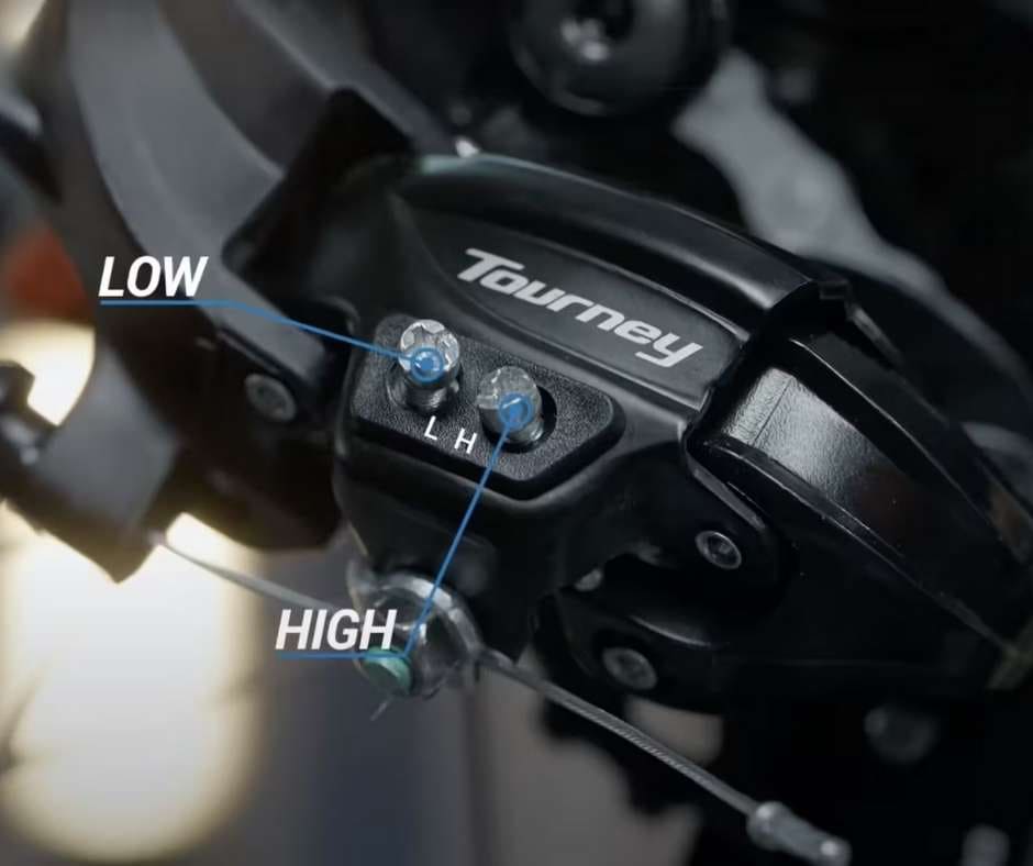 Primer plano de desviador trasero Shimano Tourney identificando los tornillos de regulación H (High/Alto) y L (Low/Bajo) encargados de establecer los topes mecánicos para evitar salidas de cadena.