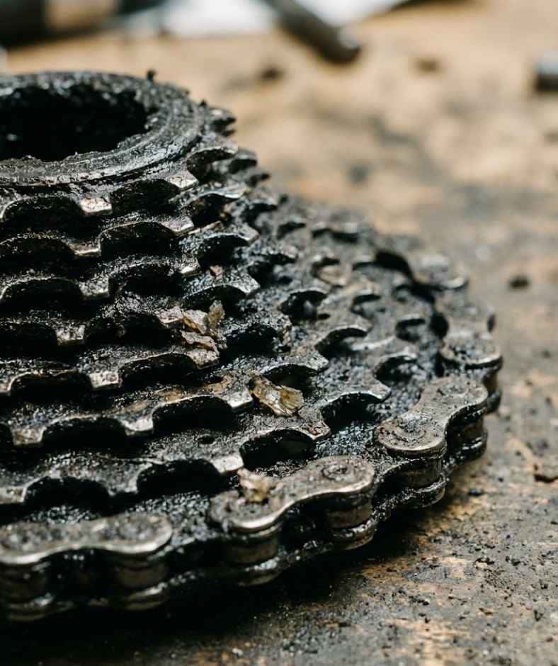 Primer plano de un cassette de bicicleta obstruido con pasta negra y suciedad acumulada, mostrando los residuos que deja el aceite o la cera mal aplicada en la transmisión.