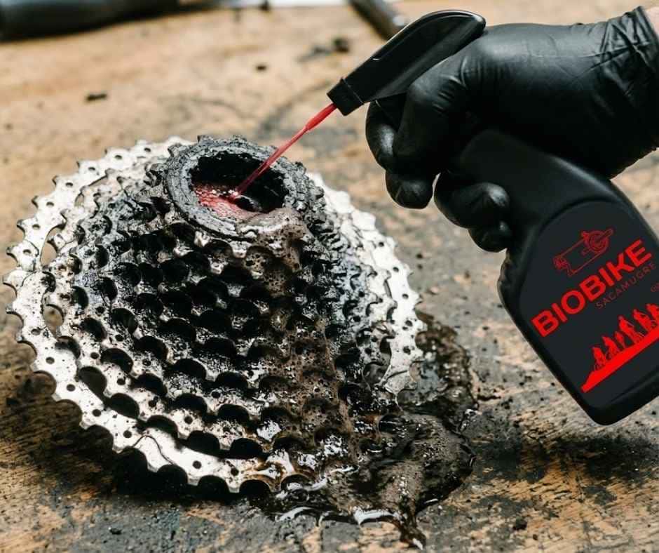Primer plano de una mano con guante aplicando desengrasante Biobike en spray directamente sobre el cassette de la bicicleta para iniciar la limpieza de la transmisión.