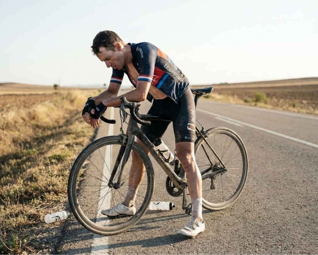 Ciclista fatigado apoyado en su bicicleta en la carretera por una pájara o hipoglucemia.